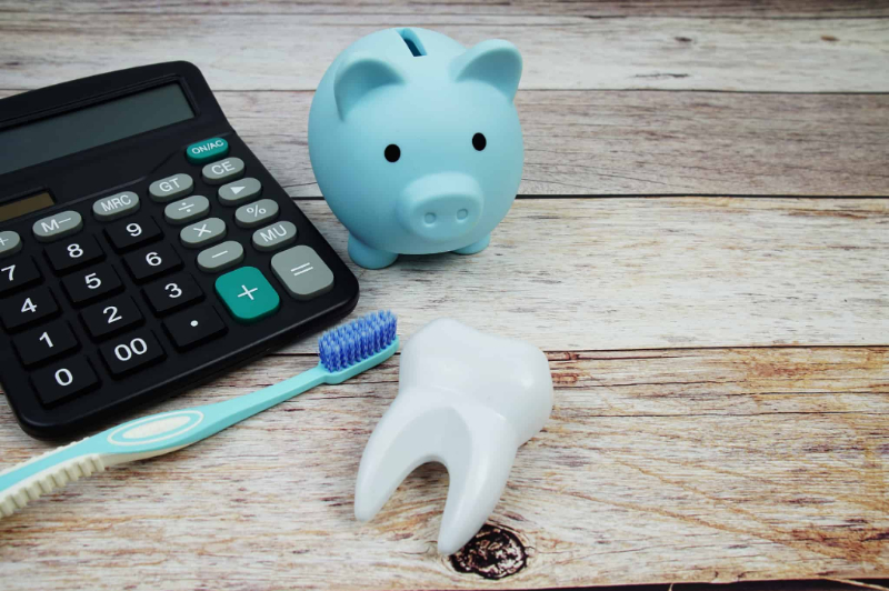 ブラッシング指導にかかる費用を示す計算機と歯ブラシと歯の模型と豚の貯金箱