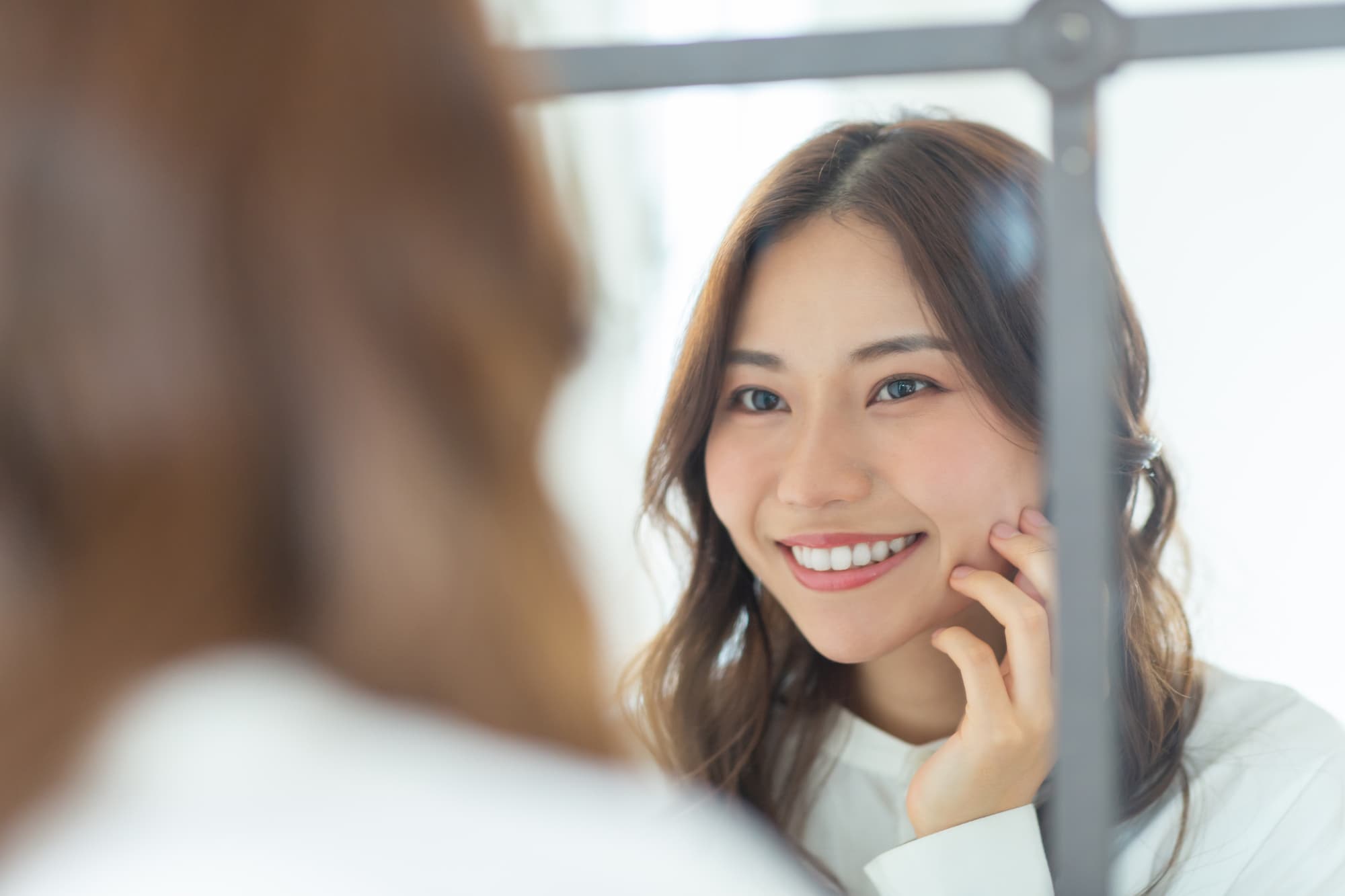 インプラント治療をした口元を鏡で確認して笑顔を見せる女性